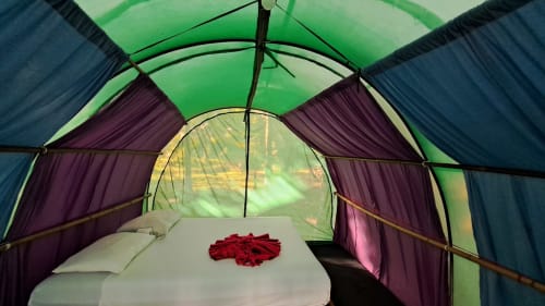 Acogedora habitación en tienda de campaña en el hostal Cayuco Maya en Bacalar con vista al lago, ropa de cama blanca y pétalos de rosa roja