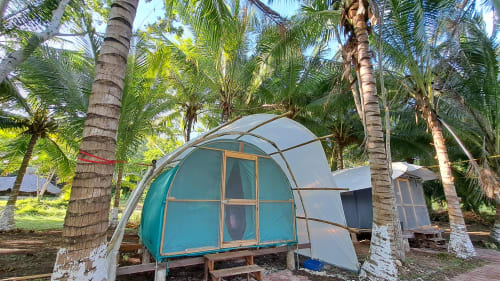 Hospedaje en tienda tipo domo turquesa rodeada de palmeras en el hostel Cayuco Maya de Bacalar, México con vista al lago