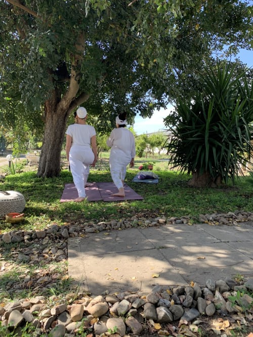 Due persone praticano yoga all'aperto sotto gli alberi ombreggiati dell'Agriturismo Il Pomo d'oro ad Assemini, Italia