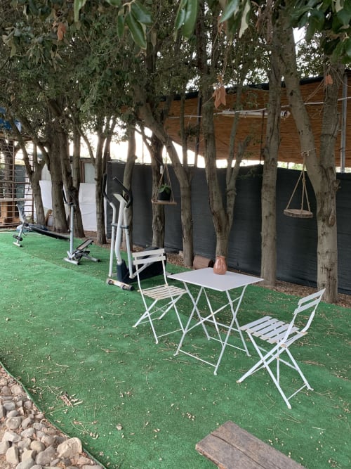 Area esterna dell'Agriturismo Il Pomo d'oro con sedie pieghevoli bianche, tavolo e attrezzi fitness sotto alberi d'ombra