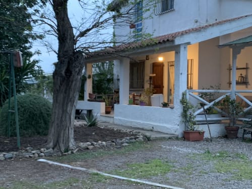 Agriturismo Il Pomo d'oro, rustico cottage bianco con portico illuminato, grande albero e vasi di piante ad Assemini