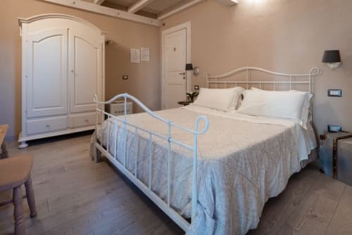 Camera spaziosa presso l'Agriturismo Il Pomo d'oro ad Assemini con letto in ferro battuto, armadio bianco e tonalità calde neutre