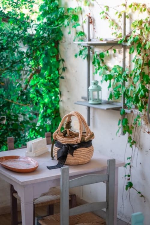 Suggestivo angolo di giardino all'Agriturismo Il Pomo d'oro con edera rampicante, tavolo in legno, cesto in vimini e ripiani ad Assemini,