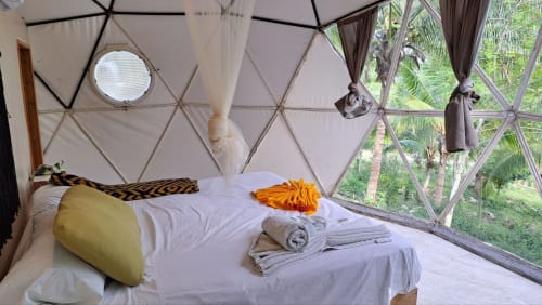 Habitación con bóveda geodésica en el hostel Cayuco Maya de Bacalar, con cama, vistas al jardín a través de grandes ventanales y decoración tropical