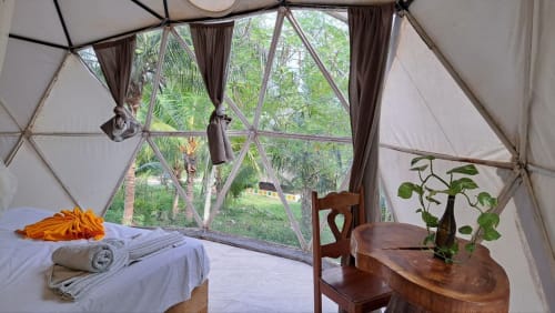 Habitación con dosel geométrico en Cayuco Maya hostel de Bacalar con vistas al jardín, cama, muebles de madera y plantas en macetas