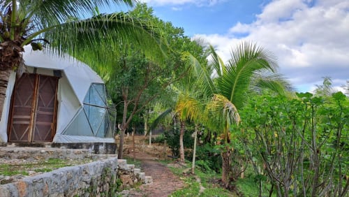 Vista del jardín del hostal Cayuco Maya en Bacalar con palmeras, vegetación exuberante y arquitectura colonial