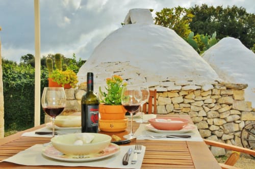 Allestimento per cena esterna al Trulli Vulés B&B di Ostuni con vino, coperto e tradizionali trulli in pietra bianca
