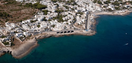 Vista aerea dell'hotel Panoramici Monolocali a Leuca con edifici imbiancati, strada costiera e Adriatico turchese