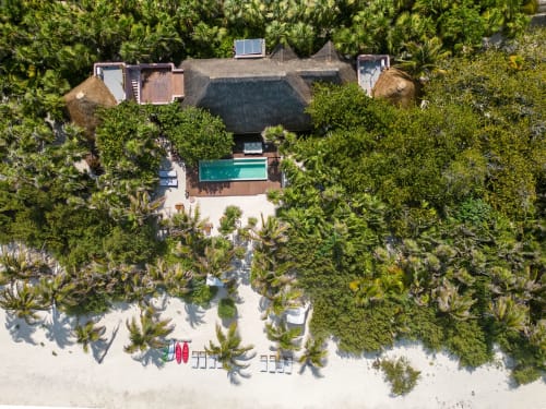 Vista aérea de villa Cantarena en Tulum con piscina turquesa, techo palapeño, playa de arena blanca y exuberante vegetación tropical