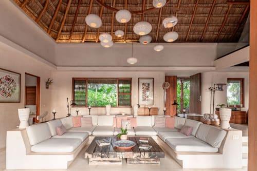 Luxurious open-concept living room in Tulum villa with cream sectional sofa, thatched ceiling, pendant lights, and views of