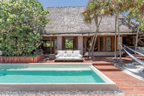 Cantarena House villa in Tulum with turquoise pool, thatched roof, white lounge seating, and tropical palm trees