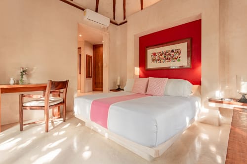Bright Tulum villa bedroom with red accent wall, queen bed, wooden furniture, and sea view at Your Private Concierge