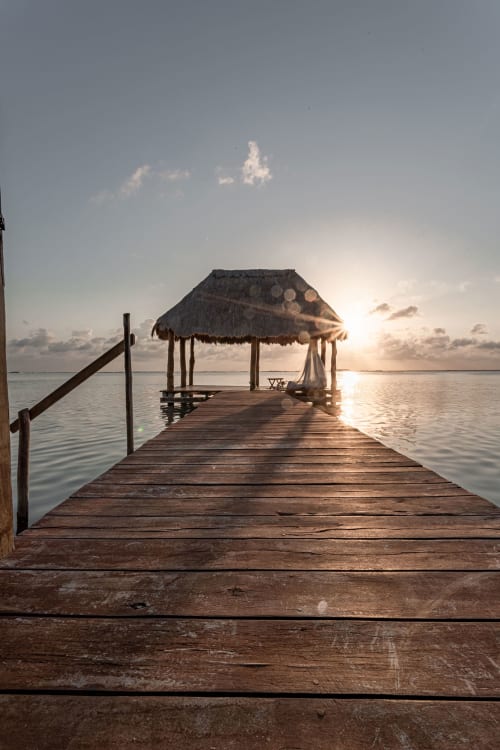Wooden dock with thatched-roof palapa at sunset overlooking calm turquoise waters in Tulum, Mexico