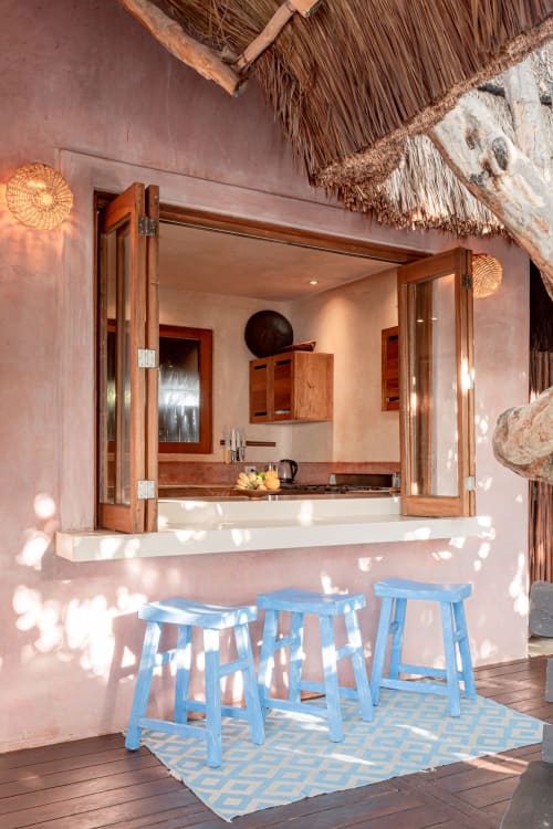 Beachfront villa kitchenette with blue bar stools, thatched roof, and pink walls in Tulum