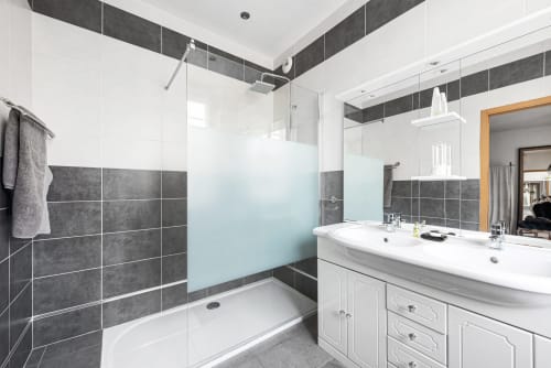 Salle de bain moderne avec murs d'accent en carrelage foncé, douche à l'italienne avec paroi vitrée, et double vasque à Au Nid De La