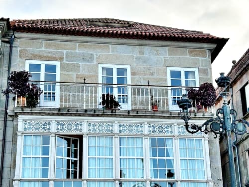 Fachada del Apartamento Boutique Solpor en Baiona con balcón con vistas al mar, ventanas azules y tejas de barro