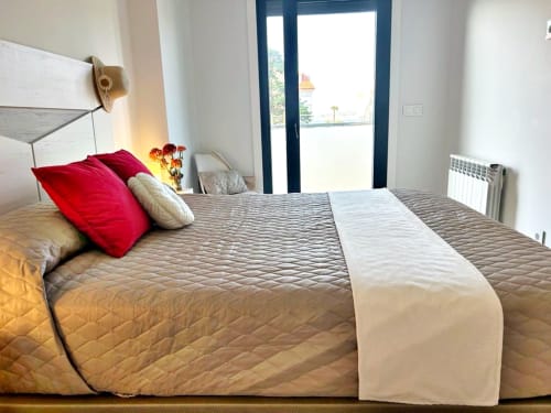Dormitorio moderno en apartamento de Baiona con cama queen, almohadas rojas, acceso a terraza y mobiliario contemporáneo