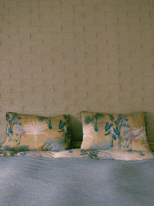 Coussins de décoration aux motifs d'oiseaux tropicaux et de feuilles de palmier sur le lit du gîte La Guirtelle à Lainsecq, France