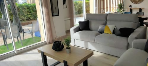 Salon moderne du gîte des Gônes avec canapé gris, table basse en bois et vue sur le jardin par les portes vitrées