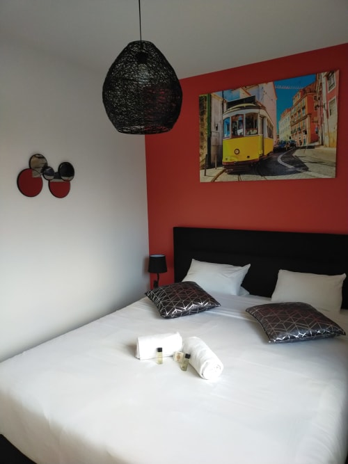 Chambre moderne du Gîte des Gônes avec mur d'accent rouge, suspension noire et photo du tram de Lisbonne jaune