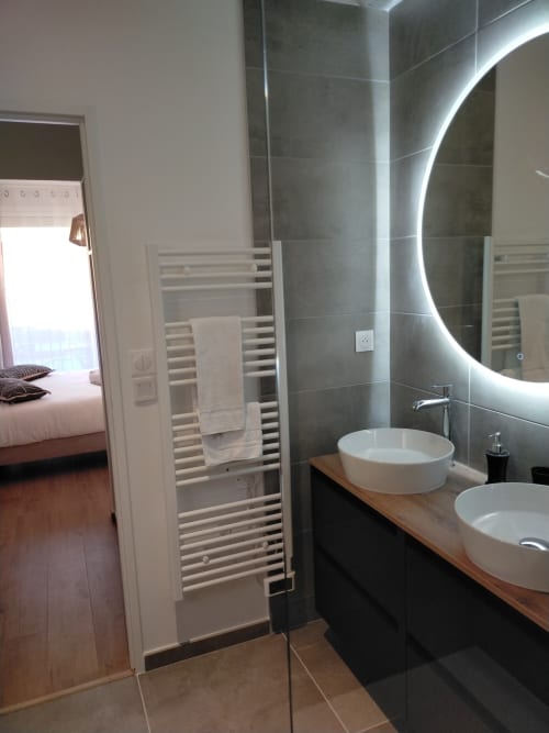 Salle de bain moderne de la villa Gîte des Gônes avec doubles vasques blanches, miroir rétroéclairé, sèche-serviettes chauffant et carrelage foncé