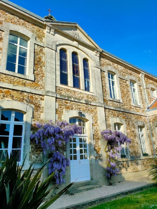 L'église en pierre de La Maison D'olivier transformée en gîte, ornée de glycine violette, portes d'entrée bleues et croix au toit