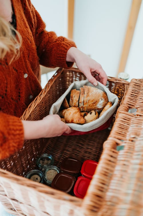Personne en pull rouille présentant pain frais et croissants d'un panier en osier aux Gîtes du Bulz, Pleyber-Christ