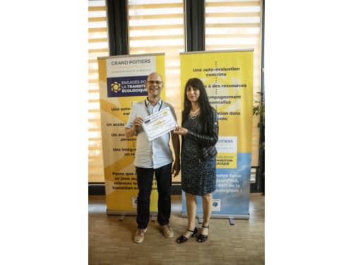Man and woman holding certificate at Grand Poitiers event with yellow banners about ecological transition in Poitiers,