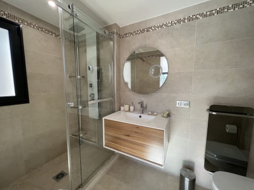 Salle de bain moderne avec douche ouverte, meuble en bois et miroir rond à la Villa La Cabane à Cap d'Antibes