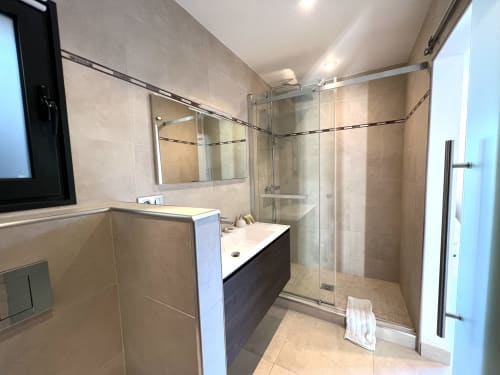 Salle de bain moderne avec vasque foncée, grand miroir et douche à effet pluie vitrée à la Villa La Cabane, Cap d'Antibes