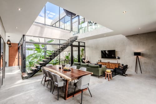 Villa moderna en Tulum con sala abierta, tragaluz, escaleras negras, mesa de comedor de madera, sofá verde y vistas al jardín exuberante