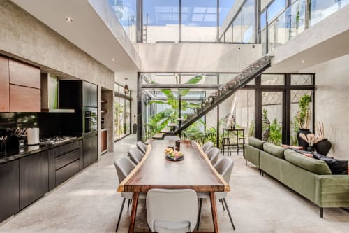 Villa moderna en Tulum con área abierta, cocina negra, sofá verde y vistas del exuberante jardín a través de paredes de vidrio