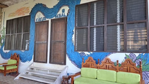 Entrada con mural azul colorido en el hostal Cayuco Maya de Bacalar, con asientos de cojines verdes y puertas de madera