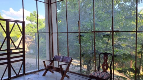 Vista del jardín desde una habitación del albergue Cayuco Maya en Bacalar, con sillas de madera y exuberante vegetación tropical visible