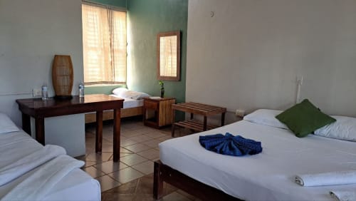 Habitación espaciosa en el hostal Cayuco Maya de Bacalar con múltiples camas, muebles de madera y detalles en verde