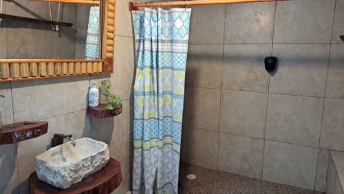 Baño rústico en el hostel Cayuco Maya de Bacalar con lavamanos de piedra, cortina de ducha estampada y paredes de azulejos
