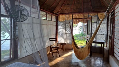 Habitación rústica en hostal Cayuco Maya, Bacalar, con hamaca, muebles de madera y vistas al lago por ventanas mosquiteras.
