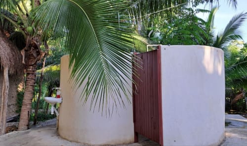 Estructuras de duchas al aire libre rodeadas de palmeras en el jardín tropical del hostel Cayuco Maya, Bacalar