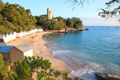 Cabines de plage blanches alignées sur le sable avec tour historique et mer turquoise à La Maison D'olivier, Mesnard La Barotiere