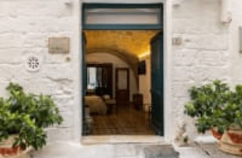 CorteLirice Paradiso entrance with dark frame doorway, white stone walls, and potted plants in Sottano 2 apartment