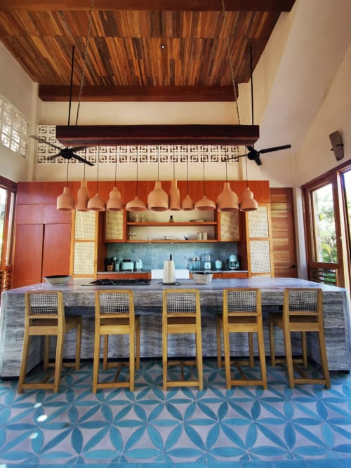 Cocina de villa moderna en Tulum con luces colgantes, barra de isla en piedra, sillas de madera y piso de azulejos geométricos azules