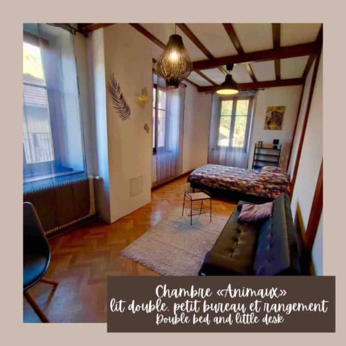 Chambre spacieuse avec lit double, poutres en bois, lampe suspendue et vue sur le jardin à Chez Lulu, Schirmeck