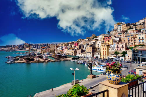 Villaggio costiero colorato con acque turchesi, barche e case sulle colline di Porto Empedocle, Agrigento, Sicilia
