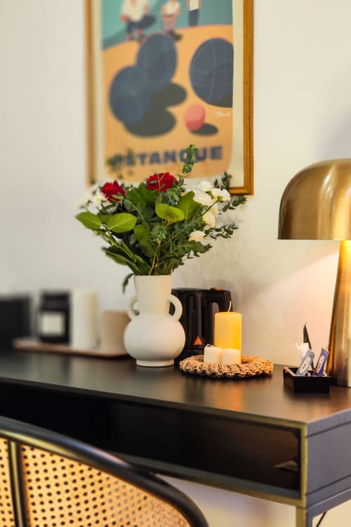 Scrivania della suite al Boutique Hôtel Provencia di Marsiglia con vaso bianco, fiori rossi e bianchi, candele e poster vintage