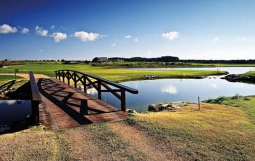 Wooden bridge over calm water at Masseria Vittoria B&B in Acaya, Vernole, Lecce, Italy, surrounded by green marshland and