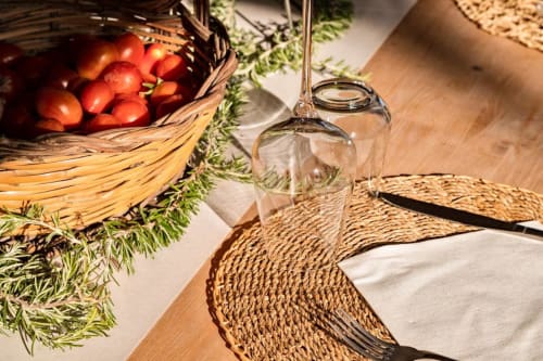 Tavolo rustico a Masseria Vittoria con pomodori freschi, erbe aromatiche, calice di vino e tovagliette intrecciate