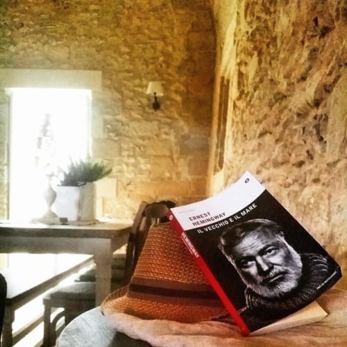 Guest holding Ernest Hemingway book in rustic stone room at Masseria Vittoria, Acaya, Italy