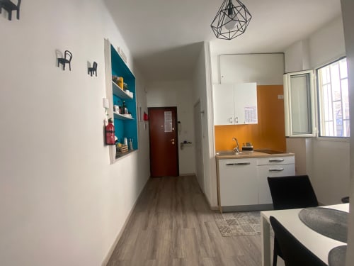 Cucina moderna e corridoio con rivestimento arancione, mobili bianchi, scaffalature azzurre e pavimento in legno presso Newhouse