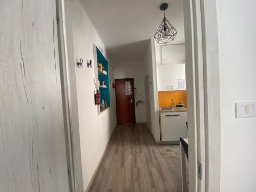 Corridoio moderno dell'appartamento Newhouse a Bari con lampada a sospensione geometrica, pareti bianche e cucina con accenti arancioni