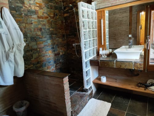 Baño espacioso en El Paraje del Chef con ducha de ladrillo, lavamanos de cerámica blanca, mampara de bloques de vidrio y tocador de madera